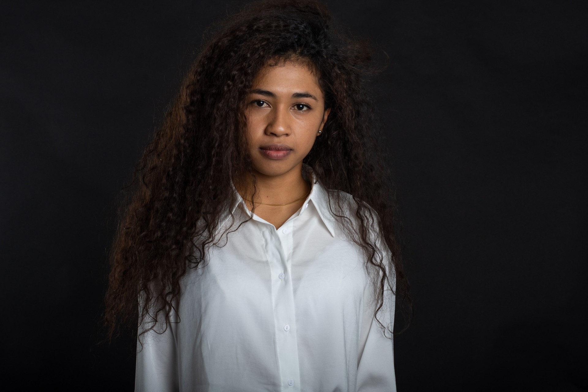 Serious young woman in white shirt looking at camera on black background